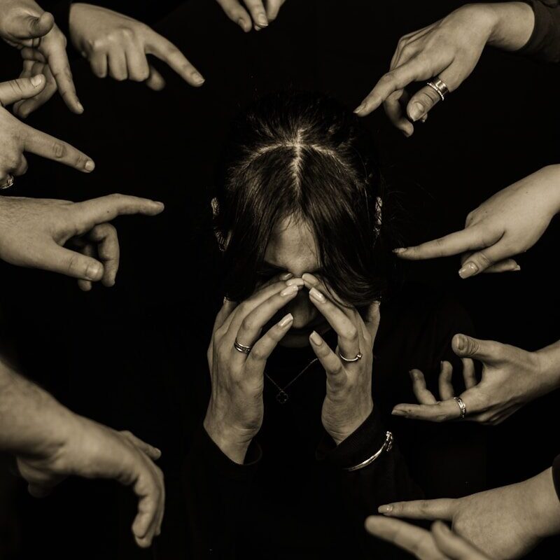 Person surrounded by pointing fingers in dark setting
