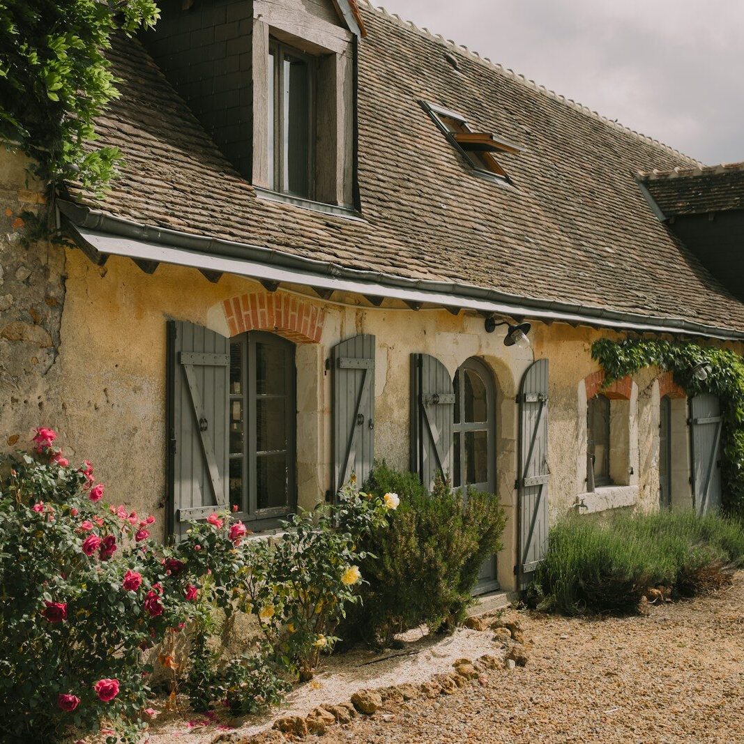 Charming stone cottage with blooming roses and shutters.